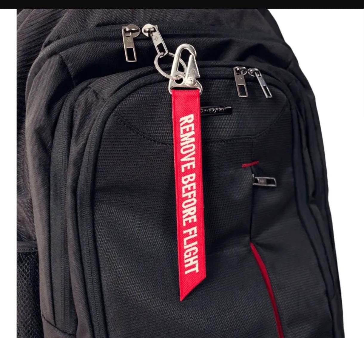 Chaveiro vermelho Remove Before Flight com mosquetão, aplicado a uma mochila